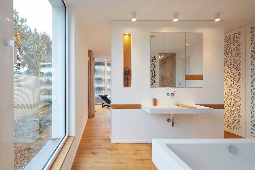 Example of a huge trendy master medium tone wood floor bathroom design in Cologne with flat-panel cabinets, a wall-mount toilet, a console sink, solid surface countertops, white cabinets and white walls