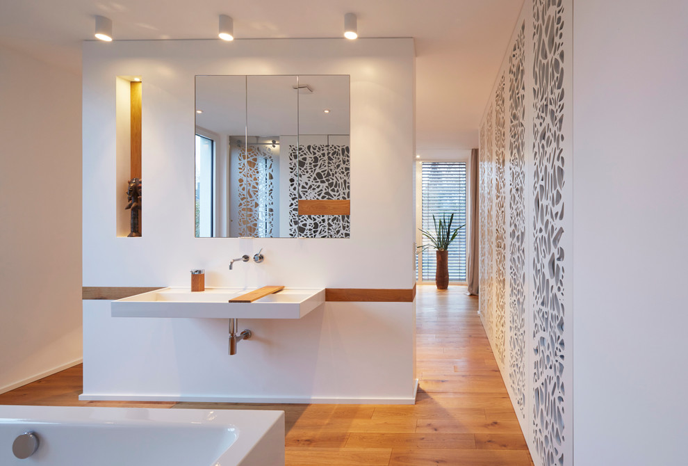 Photo of a large contemporary shower room bathroom in Cologne with flat-panel cabinets, a freestanding bath, a built-in shower, a wall mounted toilet, brown walls, medium hardwood flooring, a console sink, solid surface worktops, brown floors, a sliding door and white cabinets.