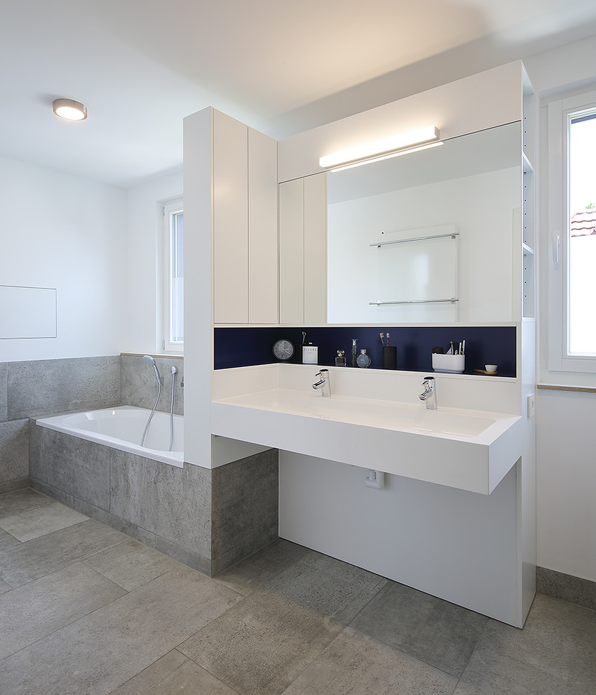 Medium sized modern ensuite bathroom with a built-in bath, grey tiles, white walls, a wall-mounted sink and grey floors.
