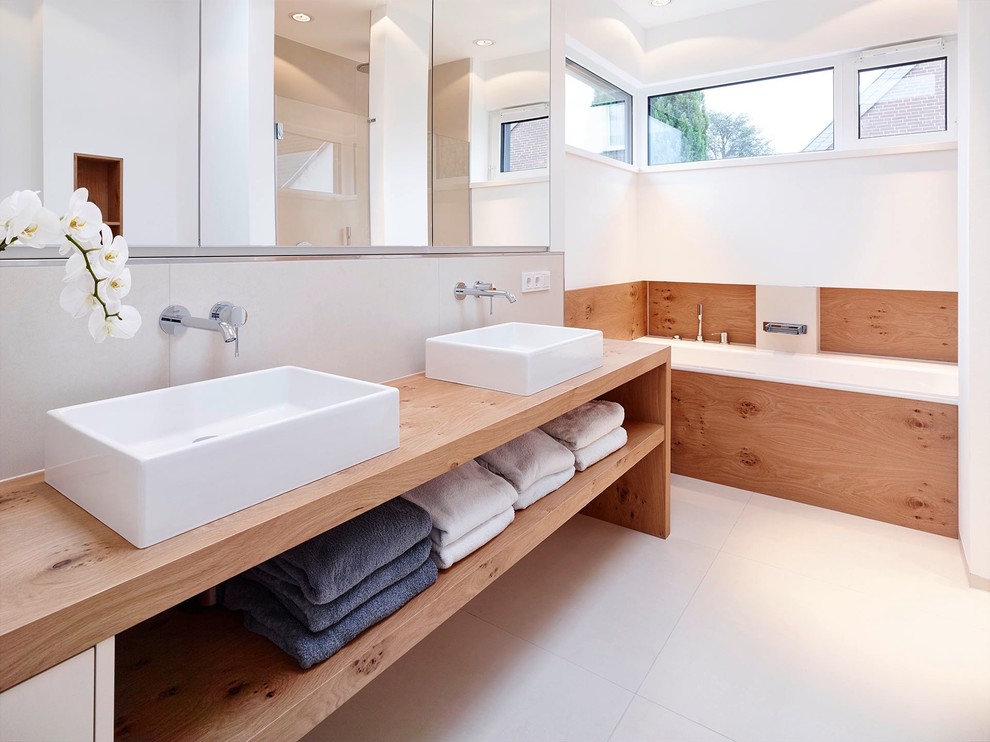 This is an example of a large modern bathroom in Dusseldorf with open cabinets, medium wood cabinets, an alcove bath, white tiles, white walls, a vessel sink, wooden worktops and brown worktops.