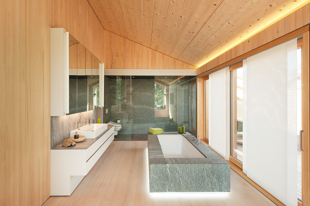 Exempel på ett mycket stort skandinaviskt badrum, med ett fristående badkar, en dubbeldusch, ett avlångt handfat, släta luckor, vita skåp, granitbänkskiva, ljust trägolv och bruna väggar