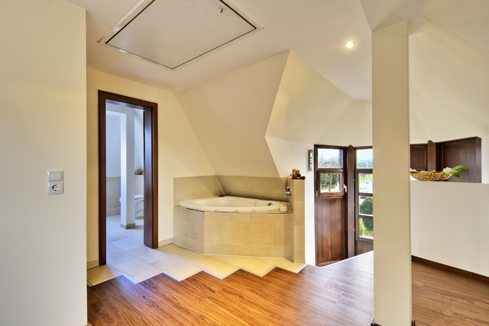 На фото: большая ванная комната в современном стиле с угловой ванной, белыми стенами и паркетным полом среднего тона с
