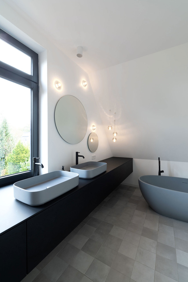 Modernes Badezimmer mit flächenbündigen Schrankfronten, schwarzen Schränken, freistehender Badewanne, bodengleicher Dusche, weißer Wandfarbe, Aufsatzwaschbecken, grauem Boden, offener Dusche und schwarzer Waschtischplatte in Hamburg