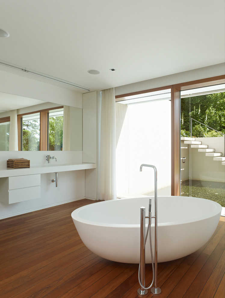 Modelo de cuarto de baño contemporáneo grande con armarios con paneles lisos, puertas de armario blancas, bañera exenta, suelo de madera en tonos medios y paredes blancas