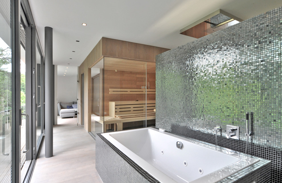 Modelo de sauna actual grande con bañera encastrada, baldosas y/o azulejos grises, baldosas y/o azulejos en mosaico, paredes marrones y suelo de madera clara
