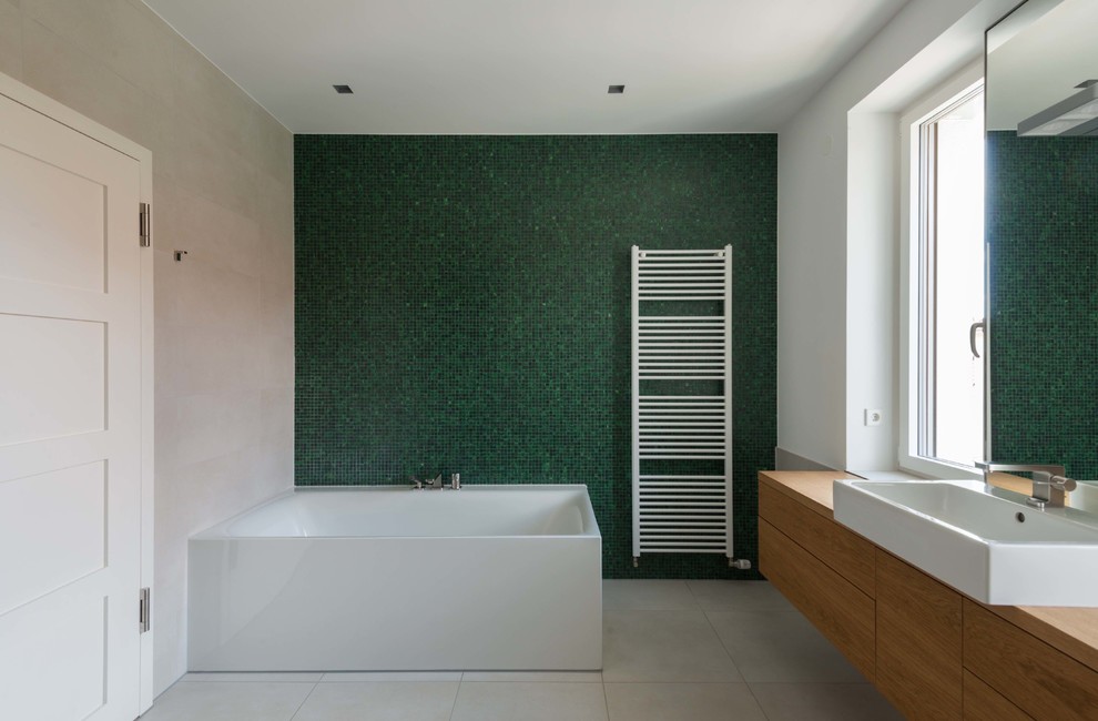 Idées déco pour une salle de bain principale moderne en bois brun de taille moyenne avec un placard à porte plane, une baignoire indépendante, un carrelage vert, mosaïque, un mur blanc, carreaux de ciment au sol, une vasque, un plan de toilette en bois et un sol beige.