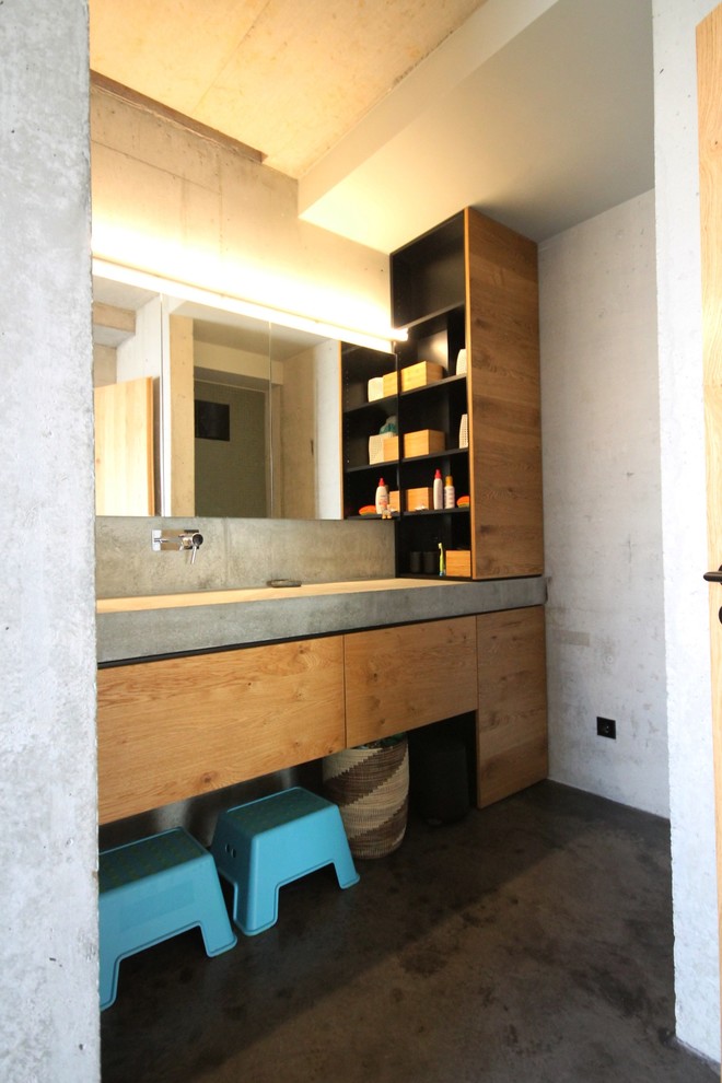 На фото: ванная комната среднего размера в стиле модернизм с серыми стенами, бетонным полом, светлыми деревянными фасадами, серой плиткой и настольной раковиной