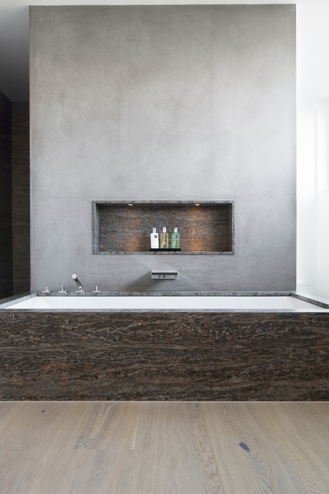 Inredning av ett modernt badrum, med ett undermonterat badkar, grå väggar, ljust trägolv, grå kakel och stenhäll