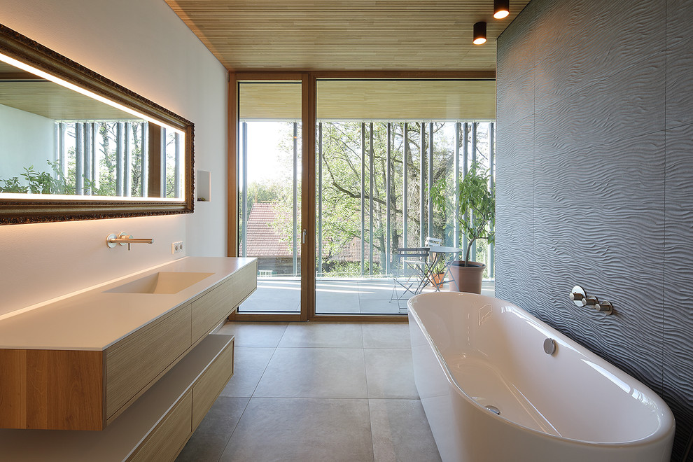 Réalisation d'une salle de bain minimaliste en bois clair avec un placard à porte plane, une baignoire indépendante, un mur blanc, un lavabo intégré, un sol gris et un plan de toilette beige.