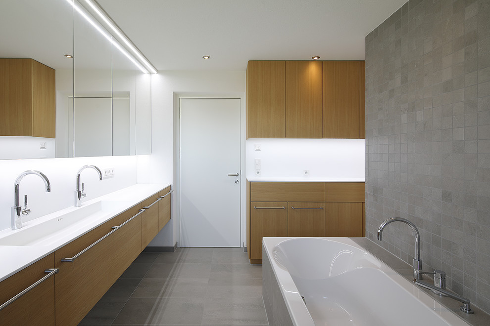 Пример оригинального дизайна: главная ванная комната среднего размера в современном стиле с плоскими фасадами, фасадами цвета дерева среднего тона, накладной ванной, серой плиткой, белыми стенами, монолитной раковиной и серым полом