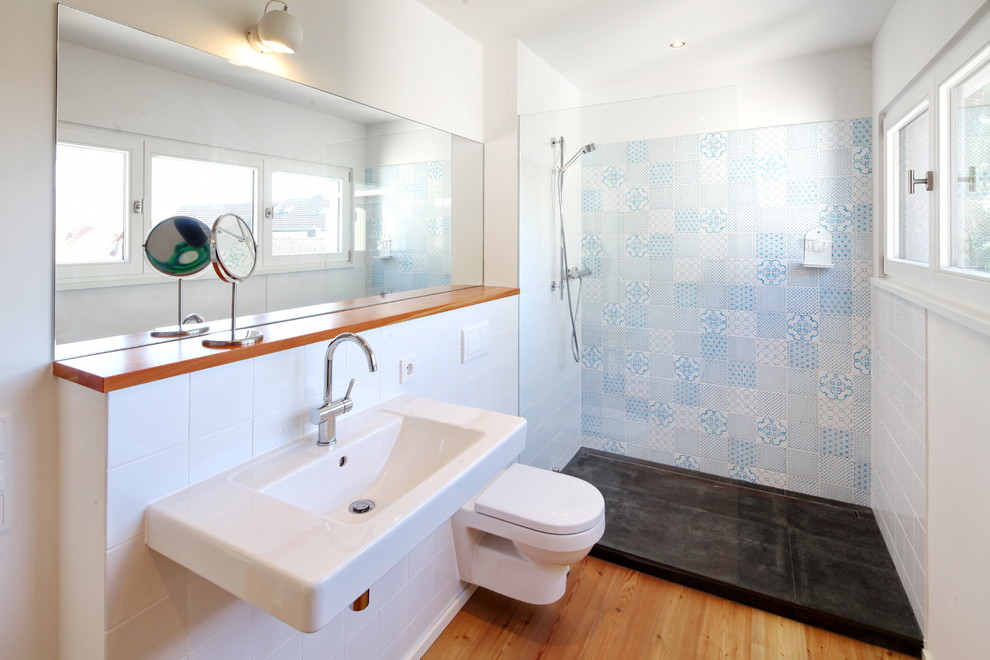 Ejemplo de cuarto de baño contemporáneo pequeño con paredes multicolor, suelo de madera en tonos medios, lavabo suspendido, ducha abierta, sanitario de pared, baldosas y/o azulejos blancos, baldosas y/o azulejos de cerámica y ducha abierta