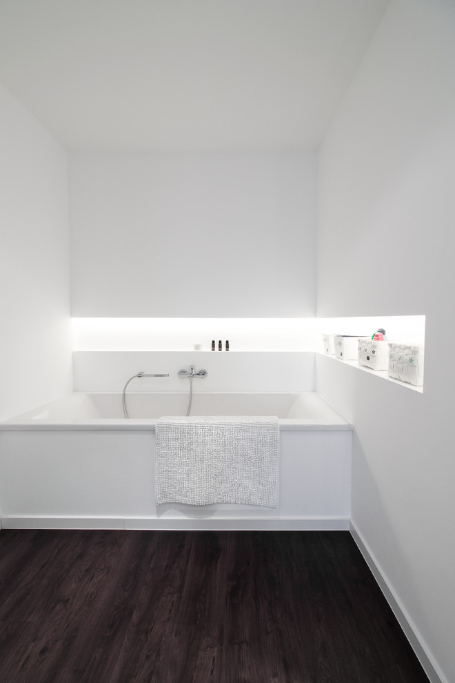 На фото: главная ванная комната в современном стиле с ванной в нише и темным паркетным полом с
