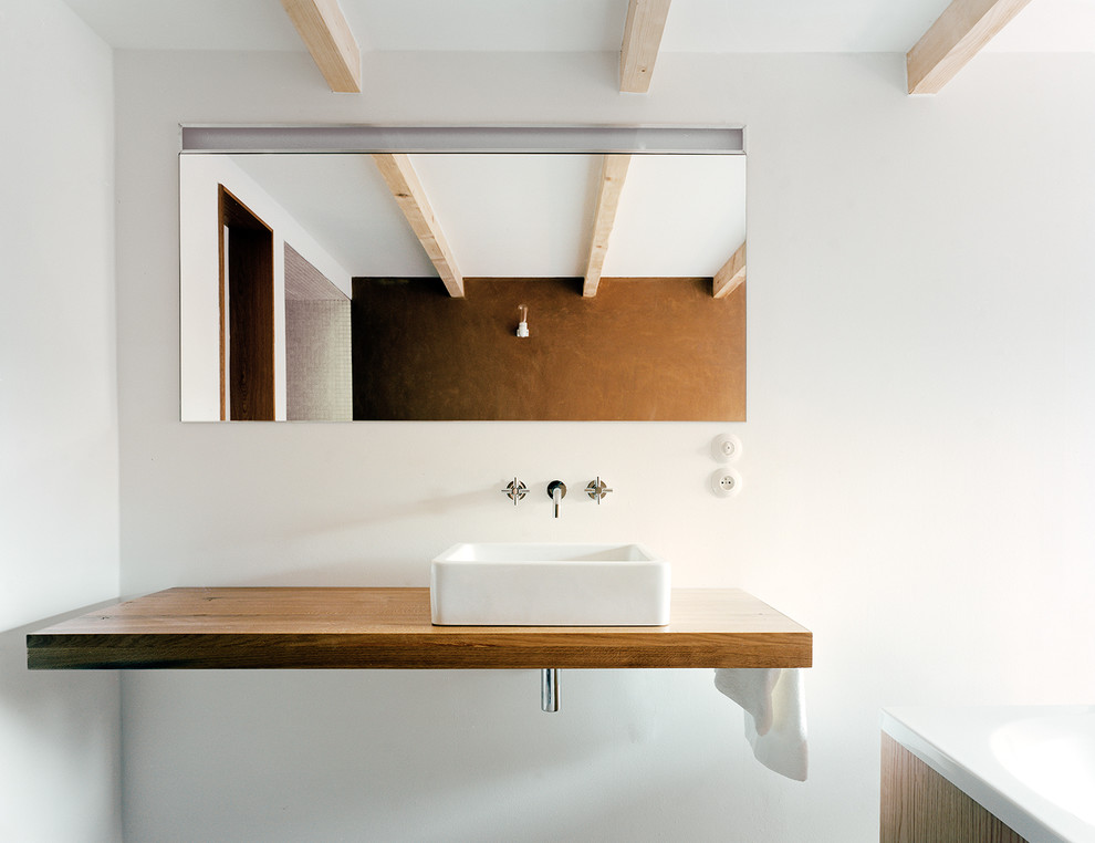 Modelo de cuarto de baño moderno con lavabo sobreencimera, encimera de madera, bañera encastrada y paredes blancas