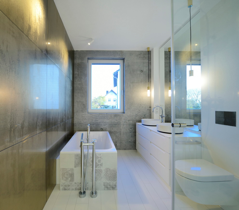 Kleines Modernes Badezimmer mit flächenbündigen Schrankfronten, weißen Schränken, Wandtoilette, weißen Fliesen, grauer Wandfarbe, Aufsatzwaschbecken und freistehender Badewanne in München