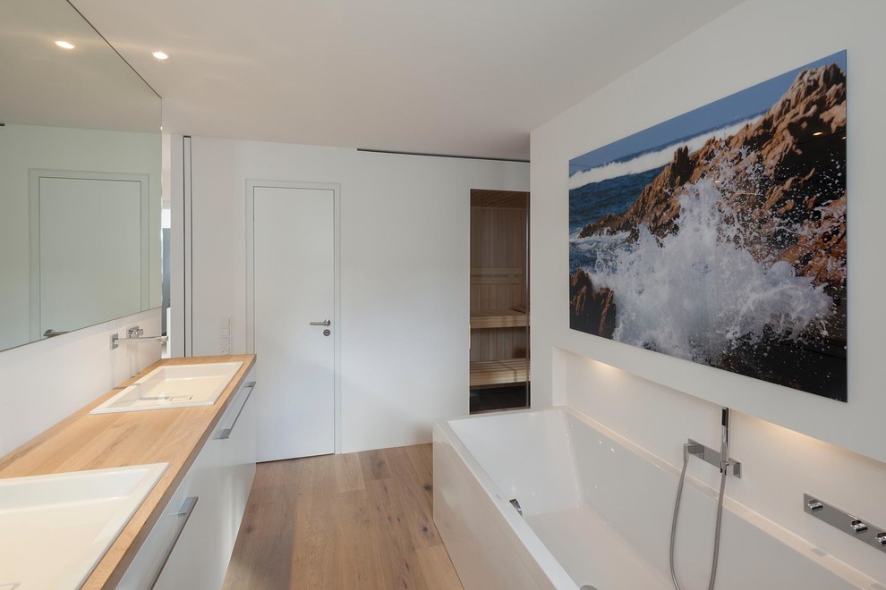 Großes Modernes Badezimmer mit Einbaubadewanne, weißer Wandfarbe, braunem Holzboden, Einbauwaschbecken und Waschtisch aus Holz in Köln