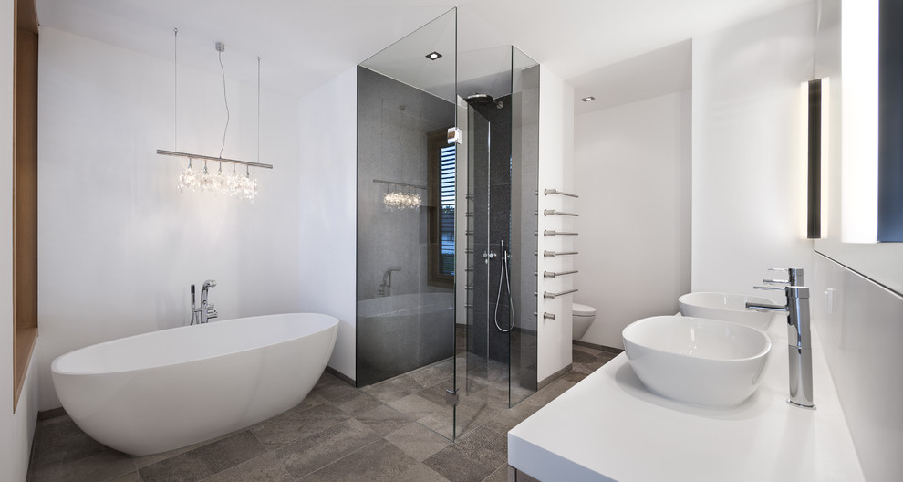 Пример оригинального дизайна: большая главная ванная комната в стиле модернизм с отдельно стоящей ванной, инсталляцией, серой плиткой, цементной плиткой, белыми стенами, полом из известняка, настольной раковиной, столешницей из искусственного камня и угловым душем