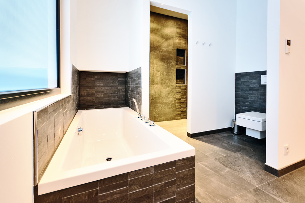 Imagen de cuarto de baño principal actual grande con bañera encastrada, sanitario de pared, baldosas y/o azulejos grises, baldosas y/o azulejos de piedra, paredes blancas y suelo de pizarra