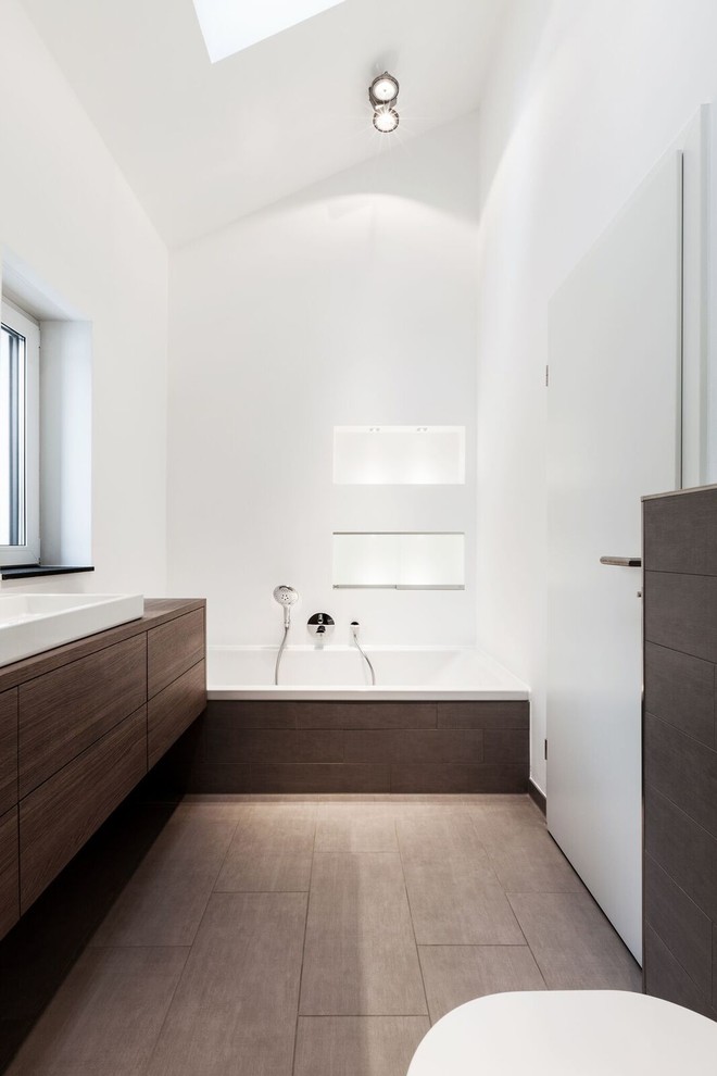 Пример оригинального дизайна: огромная ванная комната в стиле модернизм с плоскими фасадами, темными деревянными фасадами, накладной ванной, коричневой плиткой, белыми стенами, душевой кабиной, столешницей из дерева, полом из керамогранита и настольной раковиной