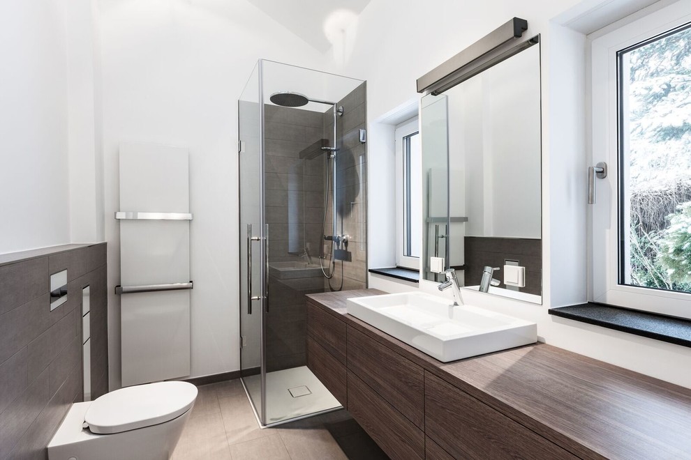 Foto på ett funkis badrum med dusch, med bruna skåp, en vägghängd toalettstol, grå kakel, vita väggar och ett fristående handfat