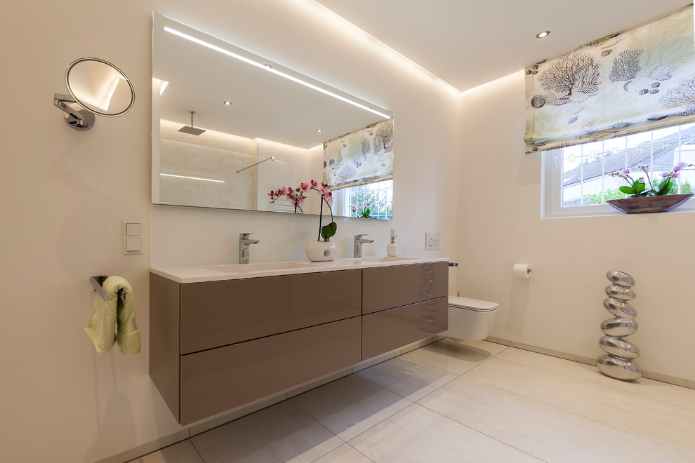 Foto di una stanza da bagno contemporanea di medie dimensioni con ante lisce, ante marroni, pareti beige, lavabo integrato, top in superficie solida, pavimento beige, WC sospeso e pavimento in cementine