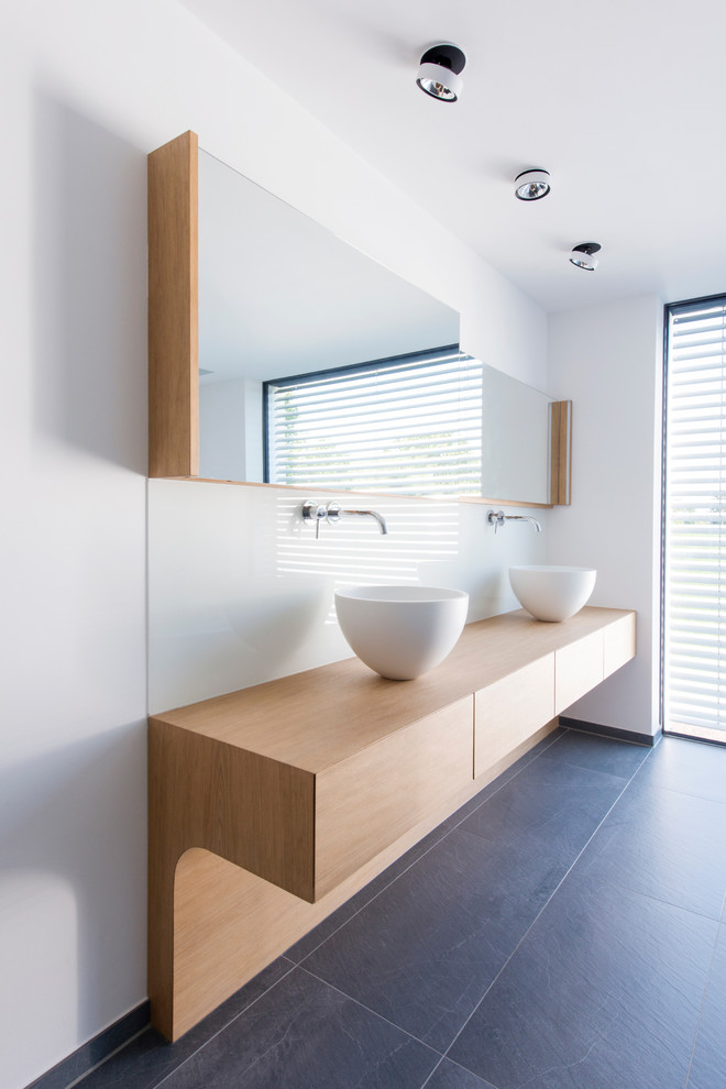 Modelo de cuarto de baño moderno con paredes blancas, bañera exenta, baldosas y/o azulejos grises y encimera de madera