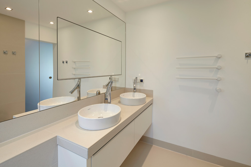 Imagen de cuarto de baño principal tradicional de tamaño medio con lavabo sobreencimera, armarios con paneles lisos, puertas de armario blancas, baldosas y/o azulejos beige y paredes blancas