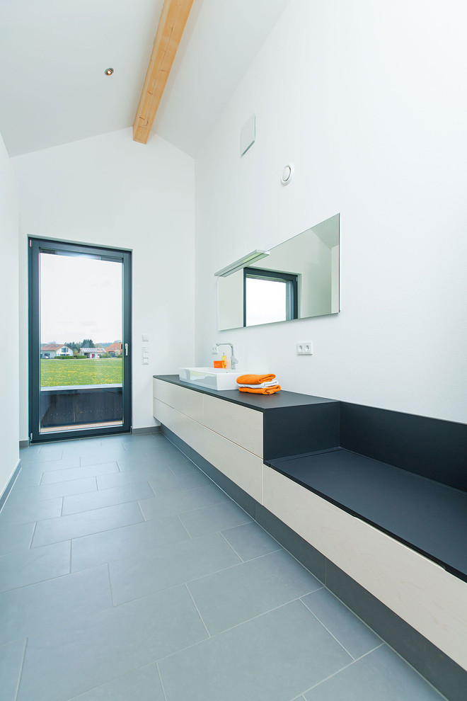 This is an example of a medium sized contemporary bathroom in Other with flat-panel cabinets, light wood cabinets, grey tiles, stone slabs, white walls and a vessel sink.