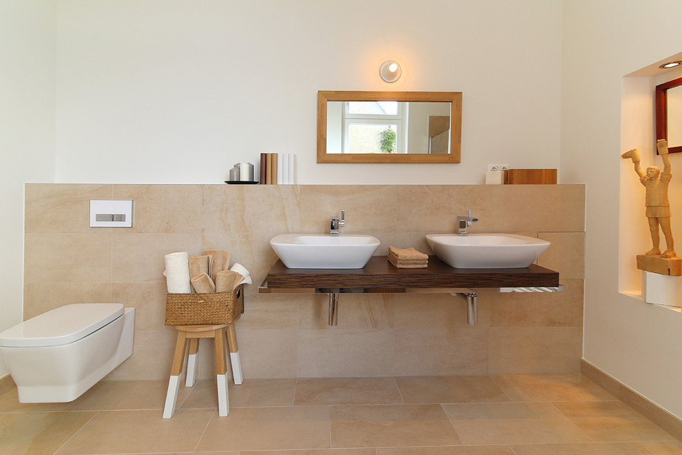 Idéer för ett mellanstort modernt badrum, med ett fristående handfat, träbänkskiva, en vägghängd toalettstol, beige kakel, beige väggar och stenkakel