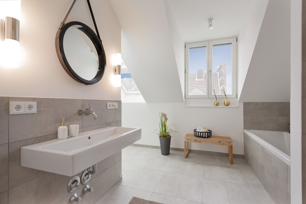 Inredning av ett modernt badrum, med ett platsbyggt badkar, grå kakel, vita väggar, ett väggmonterat handfat och grått golv