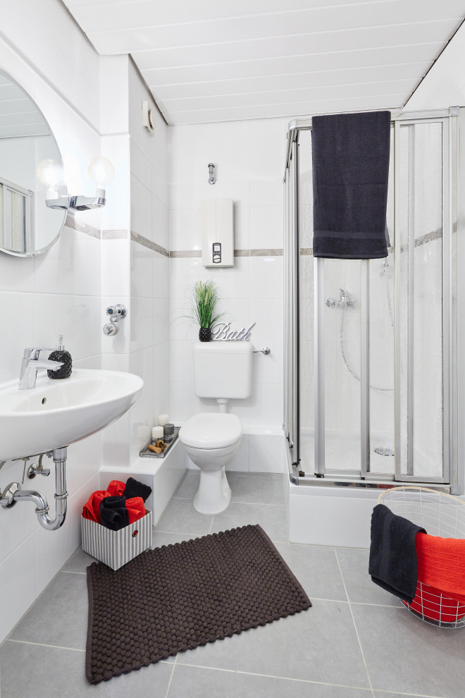 Modern inredning av ett badrum, med en hörndusch, vit kakel, ett väggmonterat handfat och grått golv