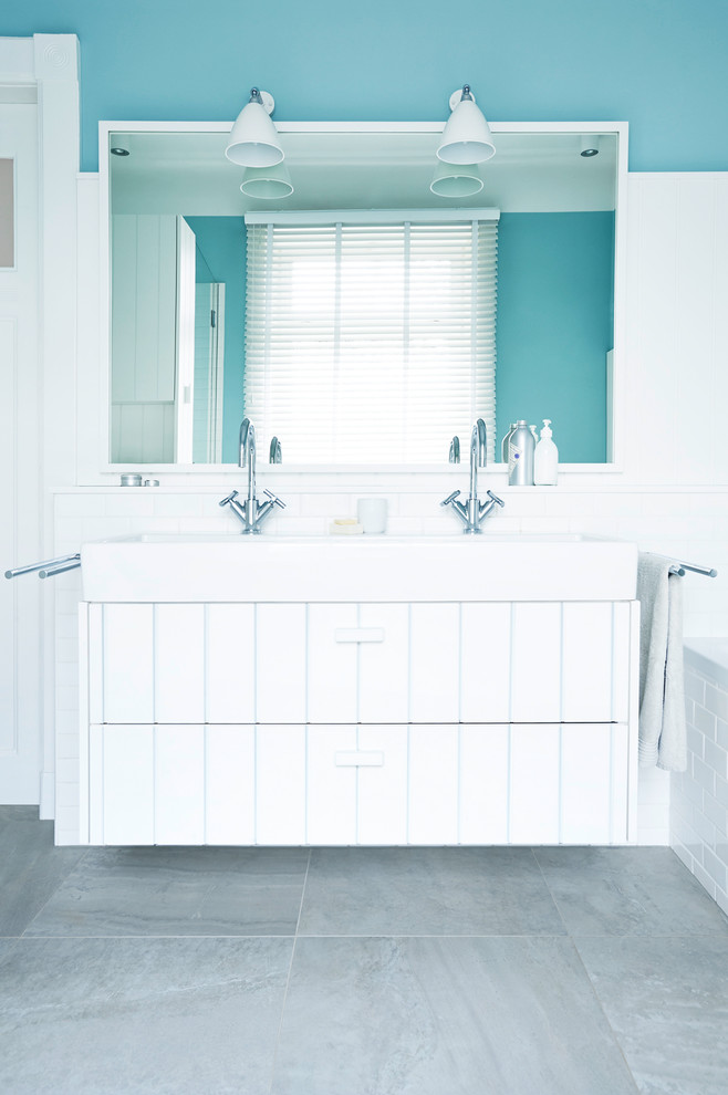 Modelo de cuarto de baño campestre con puertas de armario blancas, paredes azules, lavabo sobreencimera y suelo gris