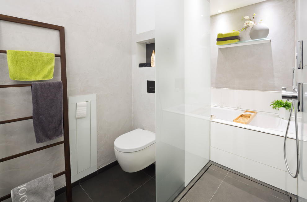 Foto på ett litet funkis en-suite badrum, med släta luckor, vita skåp, ett platsbyggt badkar, en kantlös dusch, en toalettstol med separat cisternkåpa, grå kakel, keramikplattor, grå väggar, klinkergolv i keramik, ett fristående handfat och granitbänkskiva