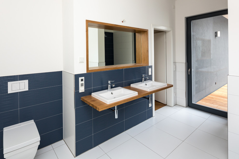 Photo of a large contemporary bathroom in Leipzig with a built-in sink, wooden worktops, blue tiles, white walls, a wall mounted toilet and ceramic flooring.