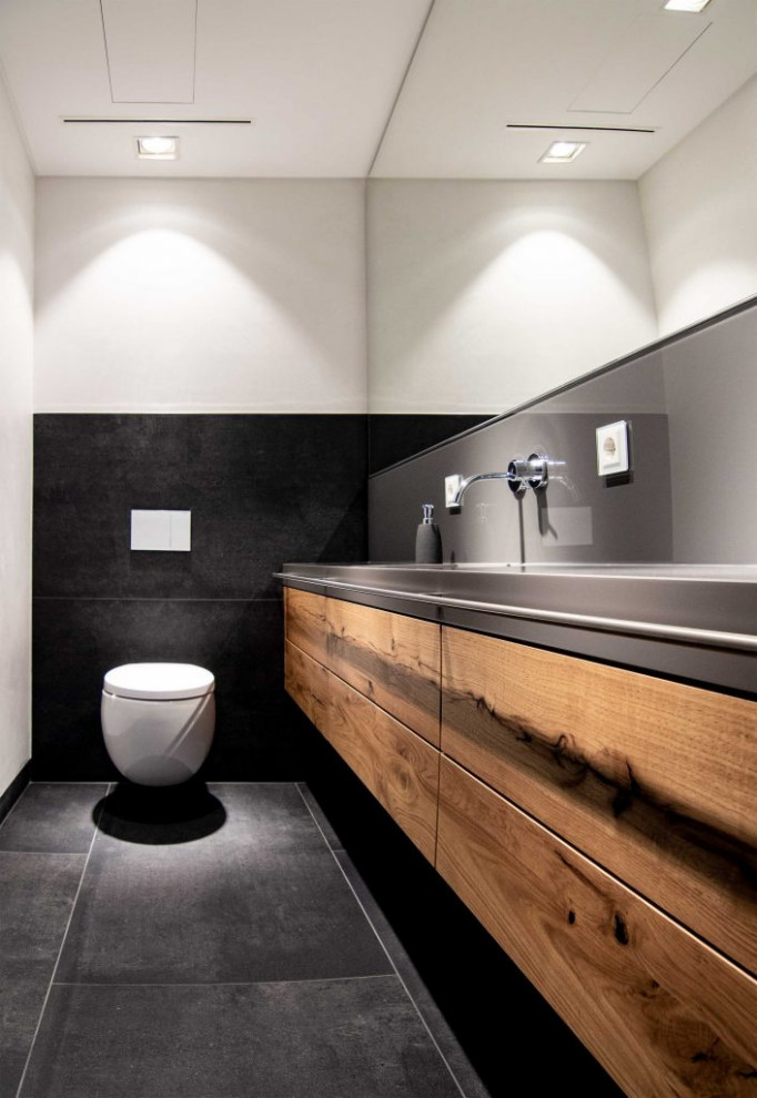 Diseño de cuarto de baño principal, único y flotante actual de tamaño medio con armarios con rebordes decorativos, puertas de armario marrones, sanitario de pared, paredes blancas, lavabo integrado, encimera de acrílico, suelo negro y encimeras grises