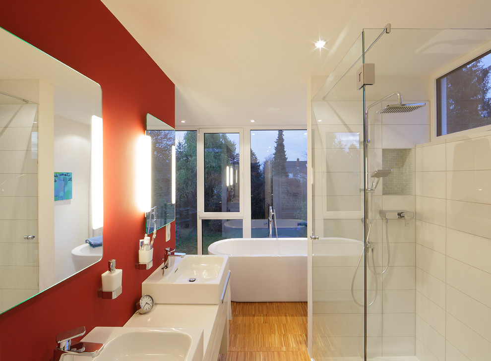 Modern inredning av ett mellanstort badrum, med ett fristående handfat, ett fristående badkar, en hörndusch, vit kakel, röda väggar, bambugolv, släta luckor, vita skåp och keramikplattor