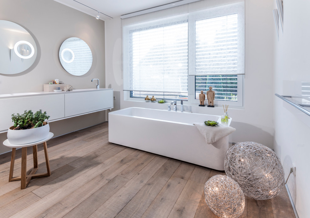 На фото: большая ванная комната в современном стиле с плоскими фасадами, белыми фасадами, отдельно стоящей ванной, белыми стенами, деревянным полом, душевой кабиной, монолитной раковиной и коричневым полом с