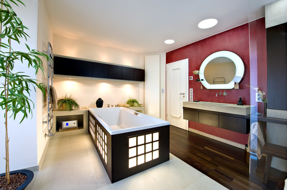 Modelo de cuarto de baño principal de estilo zen de tamaño medio con armarios con paneles lisos, puertas de armario negras, bañera exenta, paredes rojas, suelo de madera oscura y lavabo integrado