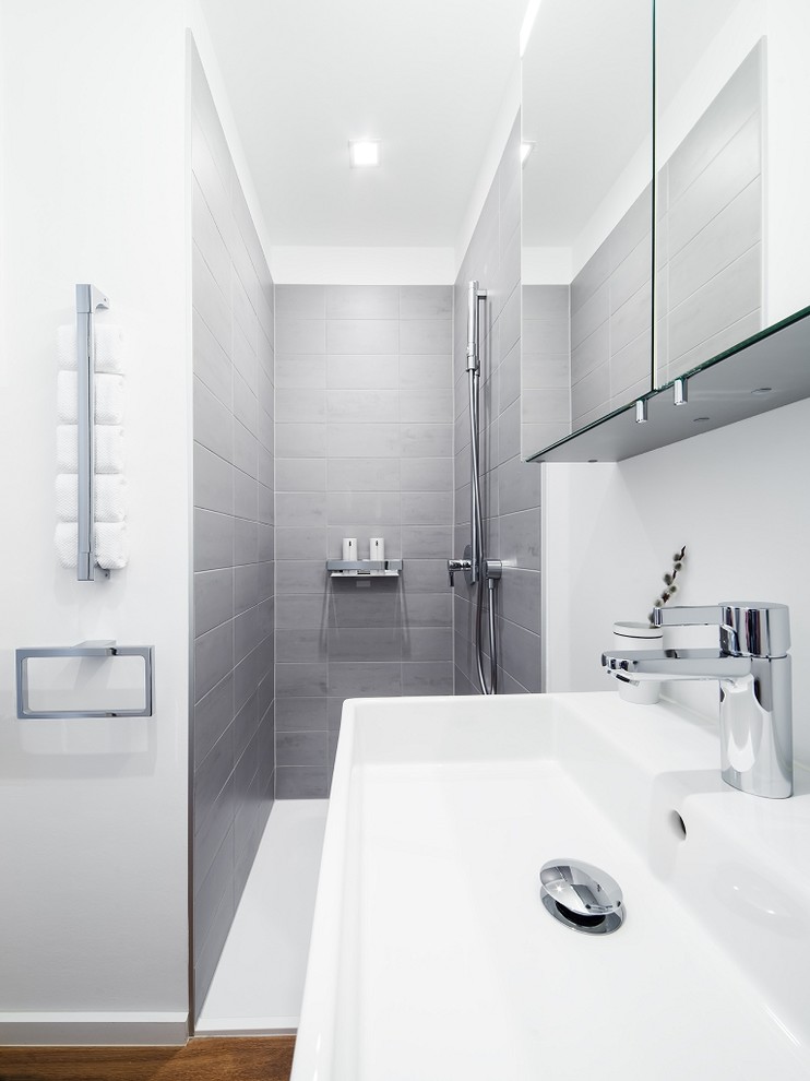 Medium sized contemporary shower room bathroom in Frankfurt with flat-panel cabinets, white cabinets, a built-in bath, an alcove shower, a two-piece toilet, grey tiles, ceramic tiles, white walls, medium hardwood flooring, a wall-mounted sink and tiled worktops.