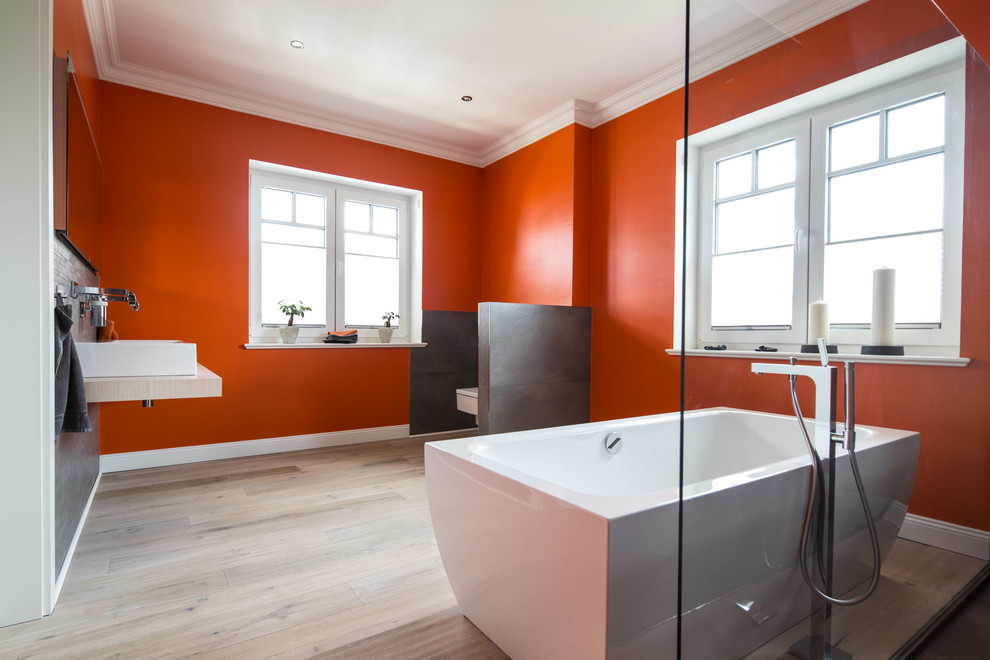 Modern inredning av ett stort badrum med dusch, med ett fristående badkar, en kantlös dusch, grå kakel, orange väggar, laminatgolv, ett fristående handfat, med dusch som är öppen, en vägghängd toalettstol och beiget golv
