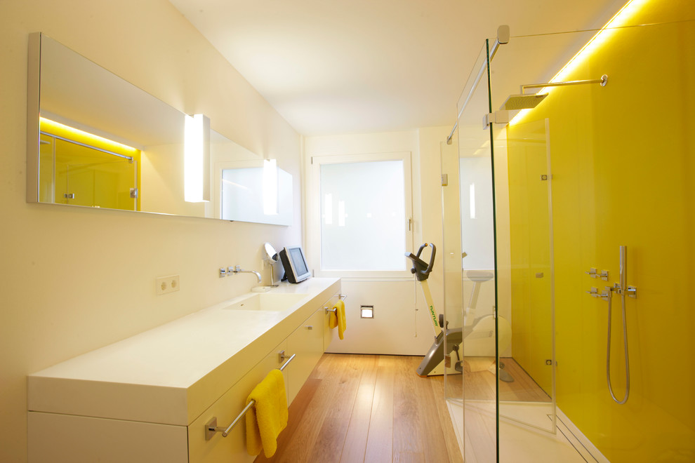 Foto på ett funkis badrum, med släta luckor, vita skåp, en kantlös dusch, gul kakel, gula väggar, ljust trägolv, ett integrerad handfat och brunt golv