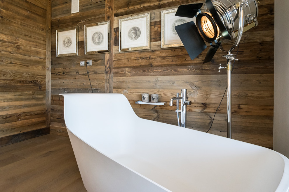 Cette image montre une salle d'eau chalet de taille moyenne avec une baignoire indépendante, un mur marron, un sol en bois brun et un sol marron.