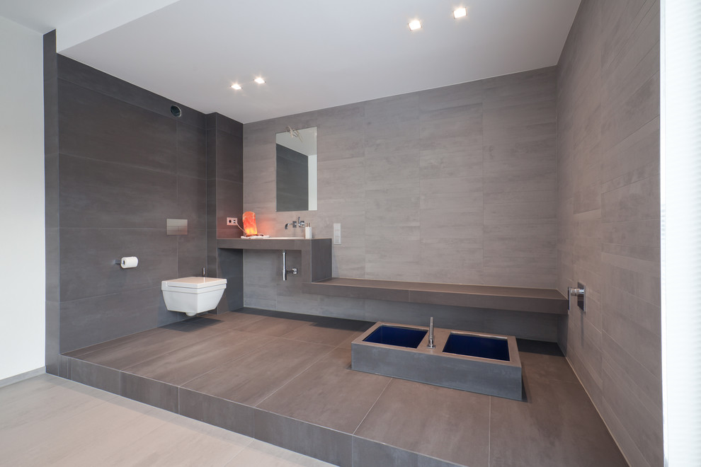 Foto de cuarto de baño contemporáneo extra grande con sanitario de pared, baldosas y/o azulejos grises, bañera encastrada, losas de piedra y lavabo encastrado