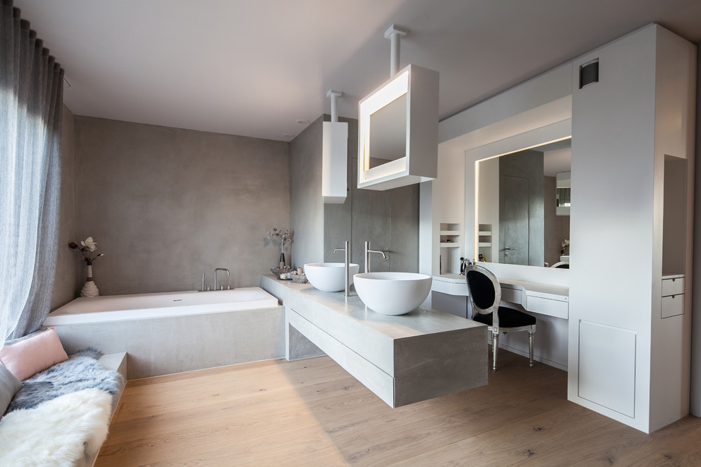Modern inredning av ett stort en-suite badrum, med ett platsbyggt badkar, grå väggar, ljust trägolv, ett fristående handfat, släta luckor, vita skåp, bänkskiva i betong, en vägghängd toalettstol, grå kakel, cementkakel och beiget golv