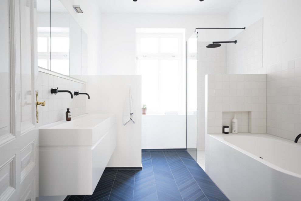 Inspiration för ett mellanstort vit vitt en-suite badrum, med släta luckor, vita skåp, ett hörnbadkar, en kantlös dusch, en vägghängd toalettstol, vit kakel, keramikplattor, vita väggar, klinkergolv i keramik, ett integrerad handfat, bänkskiva i akrylsten, blått golv och med dusch som är öppen