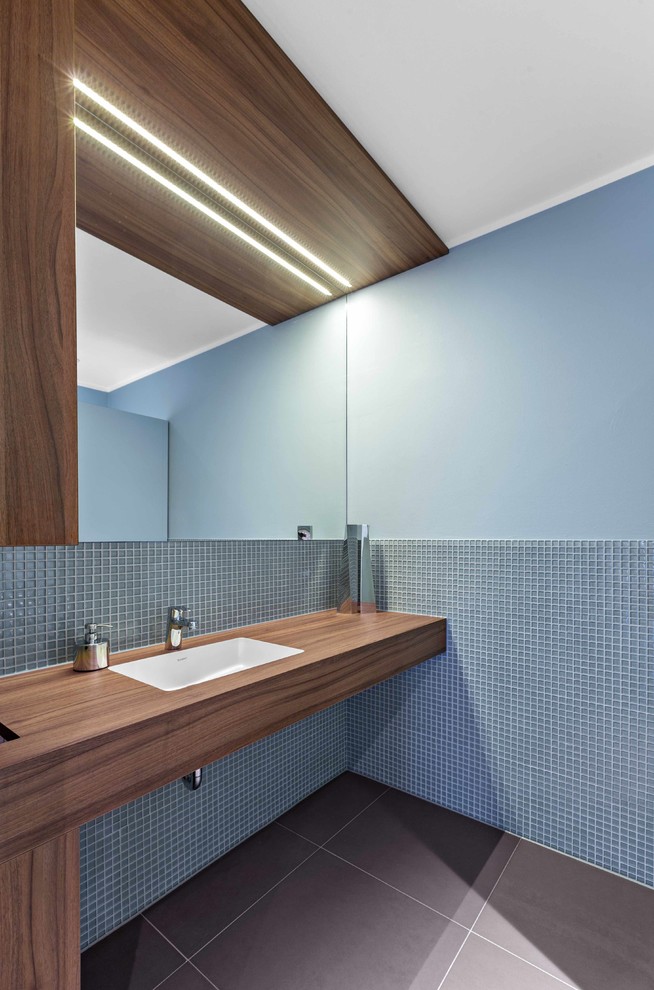 На фото: ванная комната в стиле модернизм с синей плиткой, плиткой мозаикой, синими стенами, врезной раковиной, столешницей из дерева, коричневой столешницей и зеркалом с подсветкой