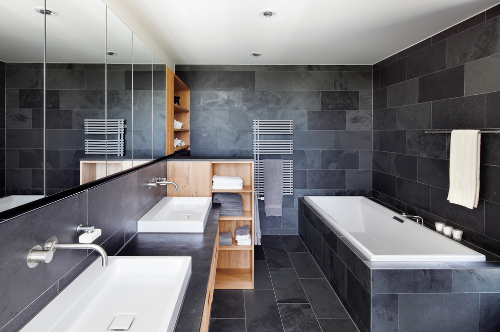 Exempel på ett stort modernt badrum, med öppna hyllor, skåp i mellenmörkt trä, ett platsbyggt badkar, grå kakel, stenkakel, grå väggar, skiffergolv och ett fristående handfat