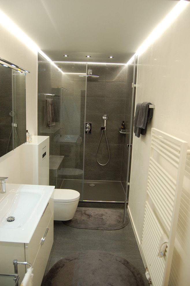 На фото: ванная комната среднего размера в стиле модернизм с плоскими фасадами, белыми фасадами, душем в нише, инсталляцией, серой плиткой, белыми стенами, душевой кабиной, консольной раковиной и столешницей из искусственного камня с