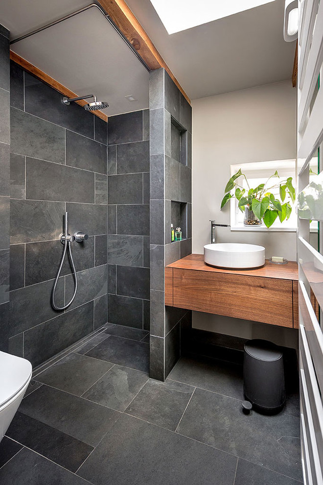 Inspiration för små moderna brunt badrum med dusch, med skåp i mörkt trä, en kantlös dusch, en vägghängd toalettstol, grå kakel, skifferkakel, grå väggar, skiffergolv, ett fristående handfat, släta luckor, träbänkskiva, grått golv och med dusch som är öppen