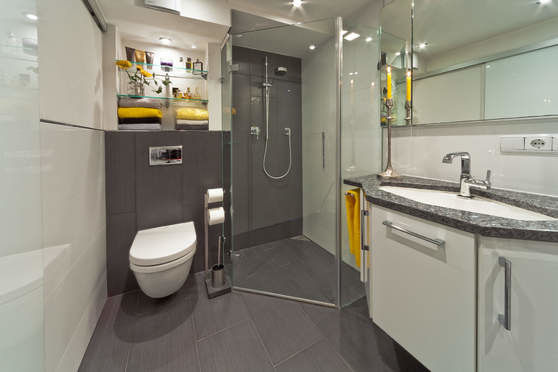 Modern inredning av ett litet badrum med dusch, med släta luckor, vita skåp, en kantlös dusch, en toalettstol med separat cisternkåpa, vit kakel, vita väggar, ett integrerad handfat, bänkskiva i akrylsten, grått golv och dusch med gångjärnsdörr