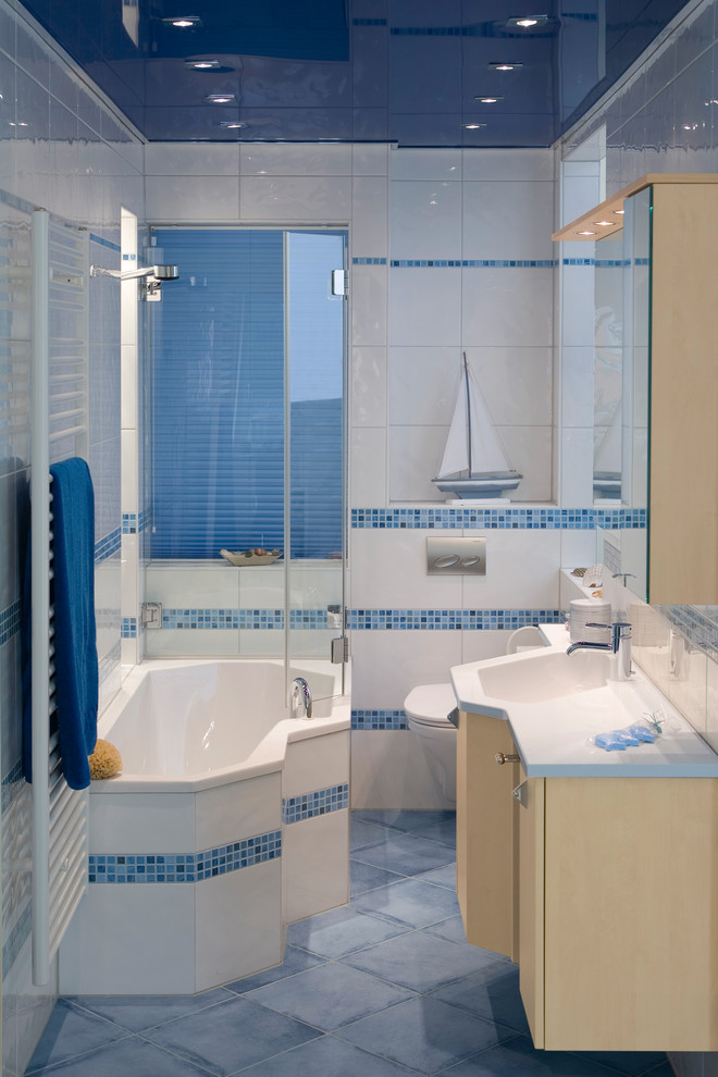 Kleines Maritimes Badezimmer mit blauen Fliesen, flächenbündigen Schrankfronten, beigen Schränken, Einbaubadewanne, Duschbadewanne, Wandtoilette mit Spülkasten, Mineralwerkstoff-Waschtisch, blauem Boden, Schiebetür-Duschabtrennung und weißer Wandfarbe in Frankfurt am Main
